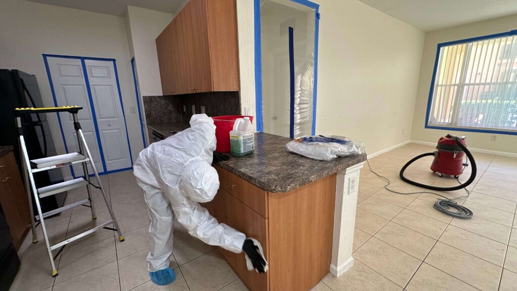 Professional Mold Remediation in West Palm Beach, FL 13 A person in a white suit scrubs mold from surfaces in a kitchen, ensuring a clean and safe environment.