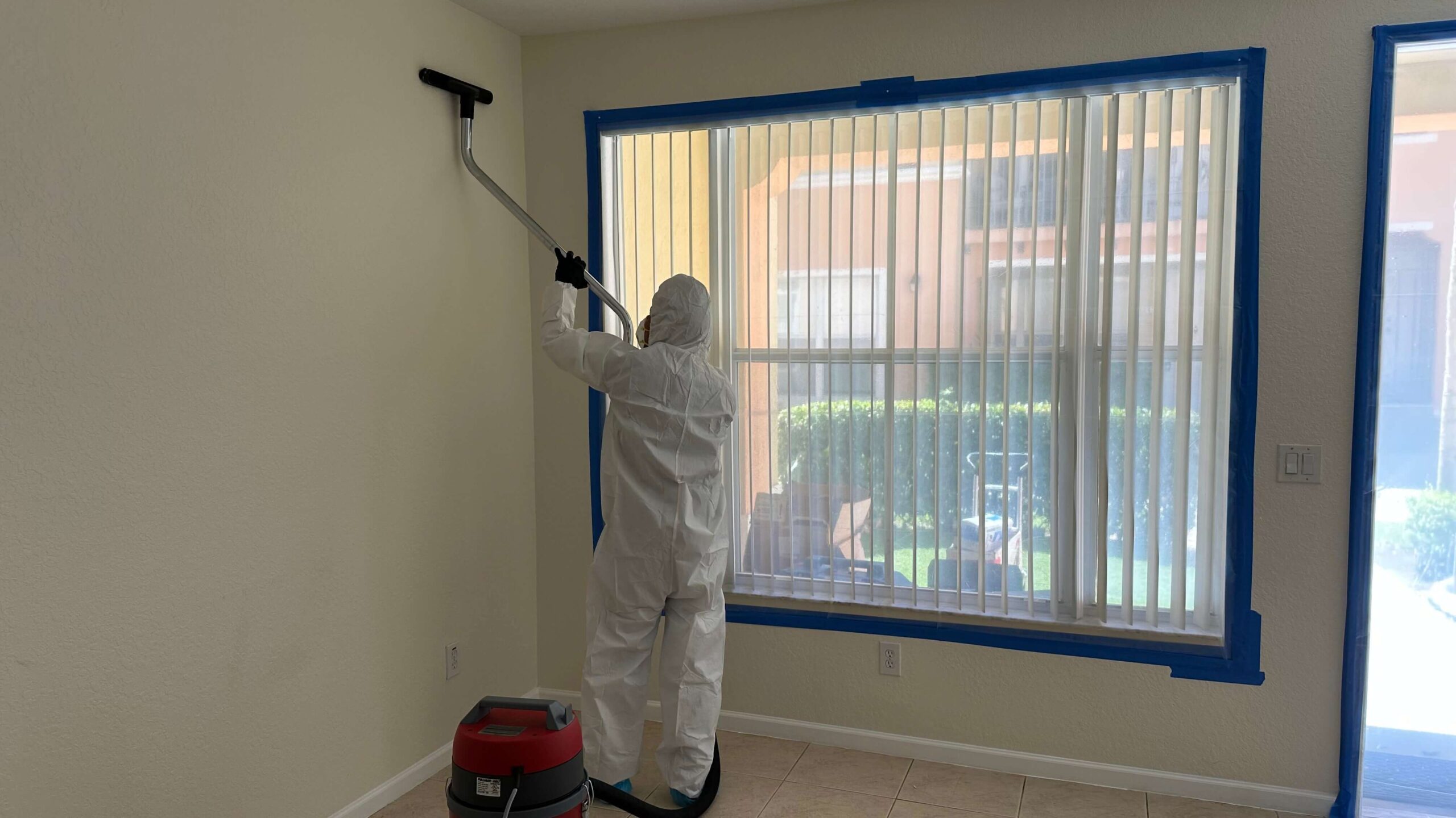 person-in-white-suit-cleaning-mold A person in a white suit and protective gear cleaning a room as part of mold cleaning efforts.